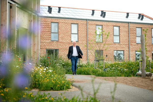 Adm direktør i plushusene martin kring går igennem bebyggelse med rækkehus og fælleshus og blomster